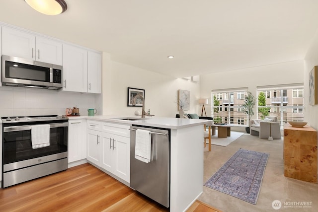 kitchen with a sink, white cabinets, a peninsula, open floor plan, and stainless steel appliances
