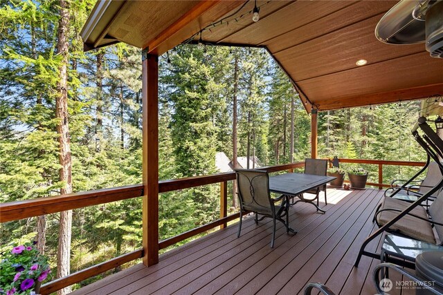 wooden terrace featuring a view of trees and outdoor dining space