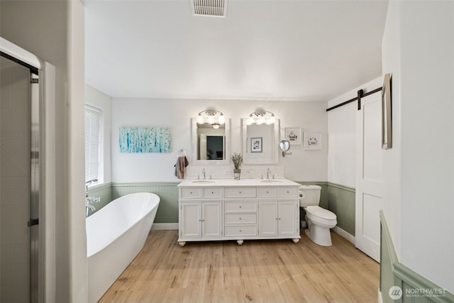 full bathroom with a sink, double vanity, a wainscoted wall, wood finished floors, and visible vents