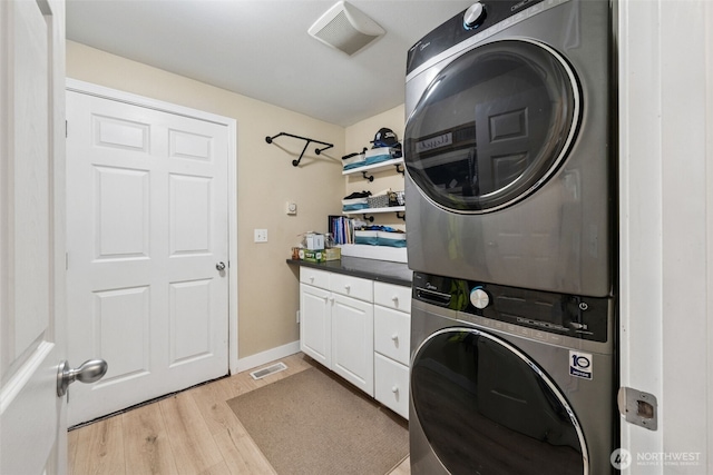 laundry area with cabinet space, visible vents, stacked washer / dryer, and light wood finished floors