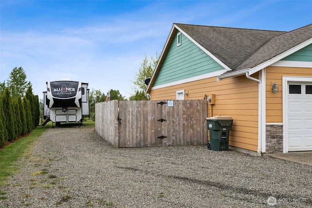 view of side of home with a garage, a shingled roof, fence, and gravel driveway
