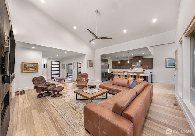 living area featuring light wood-type flooring, a ceiling fan, baseboards, and high vaulted ceiling