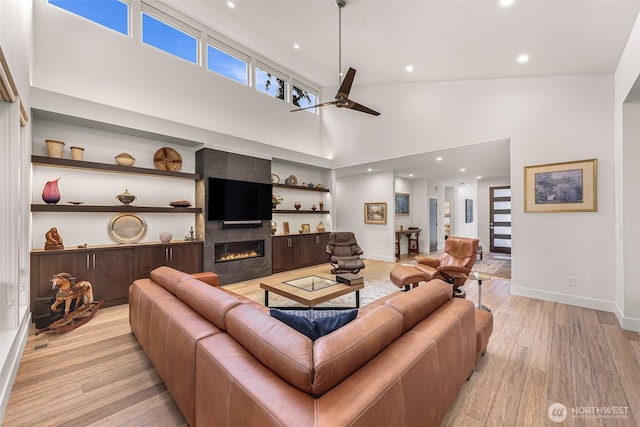 living room featuring a high ceiling, ceiling fan, light wood-style flooring, baseboards, and a tile fireplace