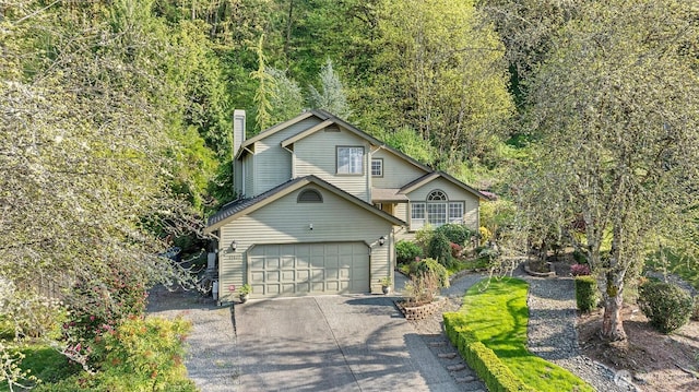 view of front of house featuring a chimney, driveway, a wooded view, and a garage