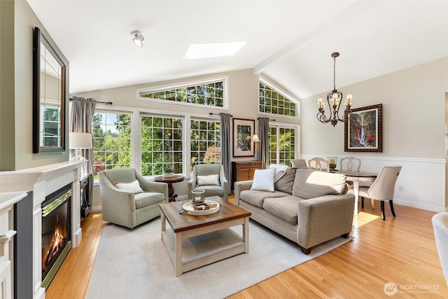 living area featuring a glass covered fireplace, light wood-style flooring, a chandelier, a skylight, and wainscoting