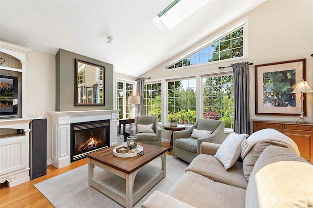 living area with a glass covered fireplace, lofted ceiling, light wood-type flooring, and a skylight