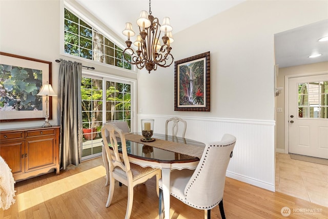 dining area featuring a chandelier, light wood-style floors, and a wainscoted wall