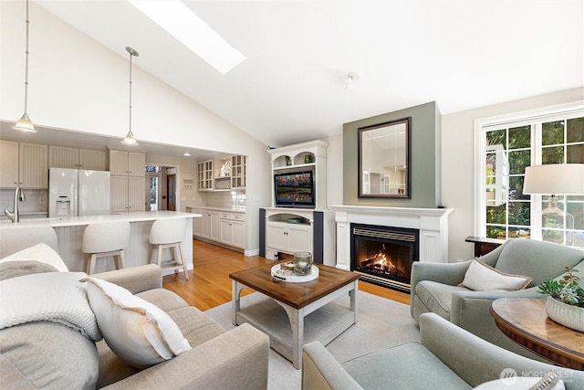 living room featuring light wood-style flooring, a lit fireplace, high vaulted ceiling, and a skylight