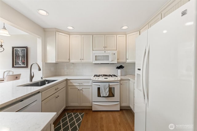 kitchen with white appliances, a sink, wood finished floors, backsplash, and light stone counters