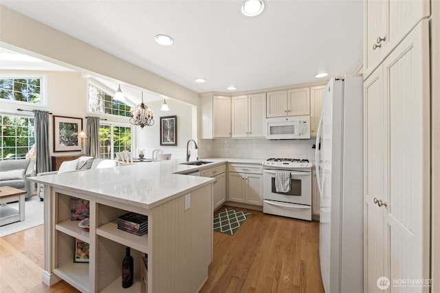 kitchen featuring white appliances, a peninsula, a sink, light wood-style flooring, and light countertops