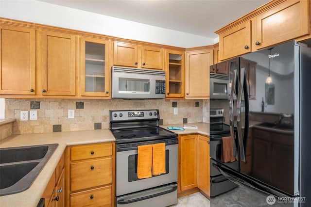 kitchen featuring appliances with stainless steel finishes, light countertops, decorative backsplash, and glass insert cabinets