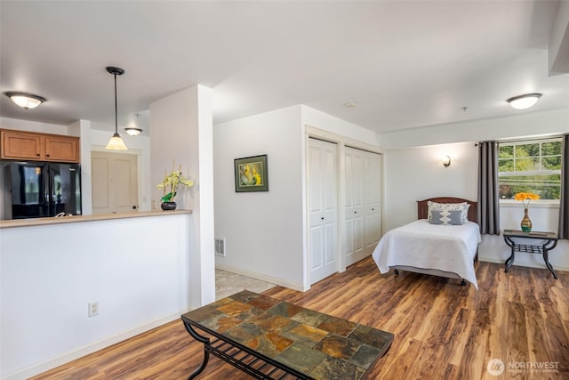 bedroom featuring freestanding refrigerator, light wood-style flooring, baseboards, and multiple closets