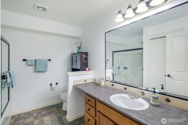 bathroom featuring a shower with door, baseboards, toilet, and stone finish floors