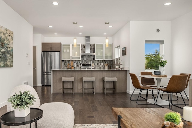 kitchen with freestanding refrigerator, wall chimney exhaust hood, a peninsula, glass insert cabinets, and light countertops