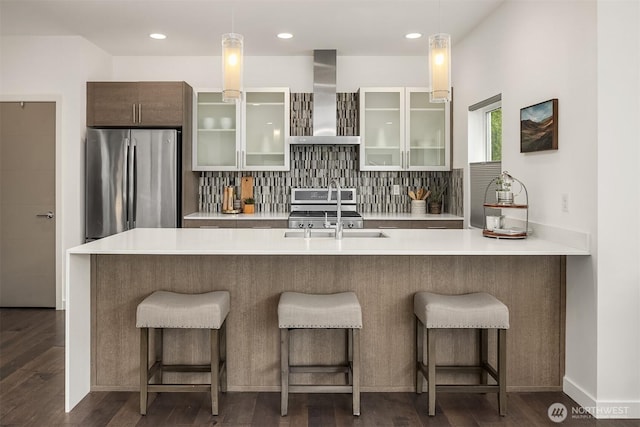 kitchen with stainless steel appliances, wall chimney exhaust hood, light countertops, pendant lighting, and recessed lighting