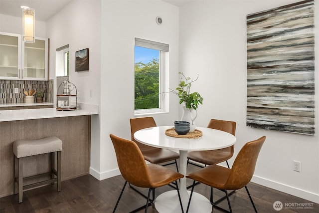 dining area featuring dark wood-style flooring, baseboards, and a bar