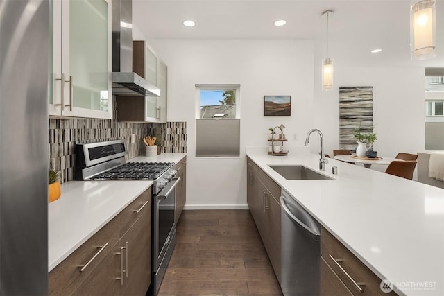 kitchen with appliances with stainless steel finishes, wall chimney range hood, a sink, light countertops, and recessed lighting