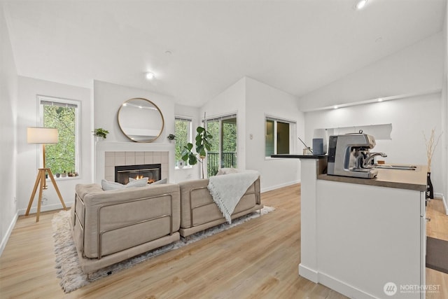 living area featuring baseboards, vaulted ceiling, light wood-type flooring, and a fireplace