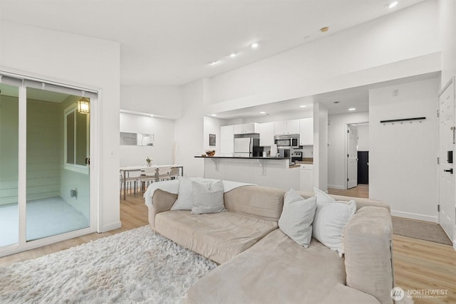 living area featuring baseboards, recessed lighting, light wood-style flooring, and lofted ceiling
