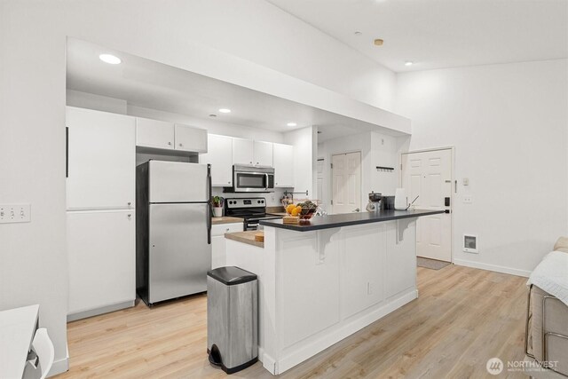 kitchen featuring appliances with stainless steel finishes, white cabinets, a breakfast bar, and light wood-type flooring