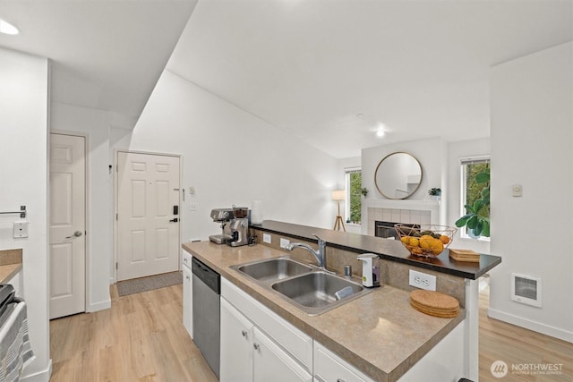 kitchen featuring a tile fireplace, dishwasher, a sink, light wood finished floors, and white cabinetry