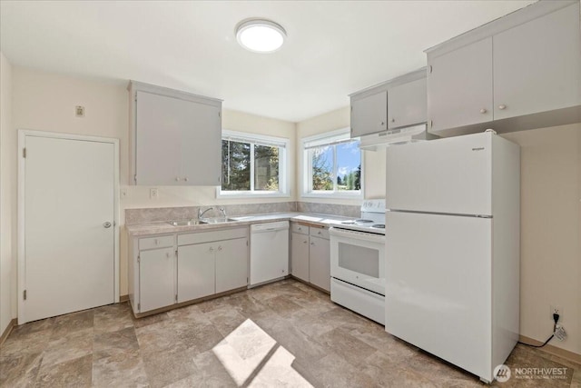 kitchen with a sink, white appliances, light countertops, stone finish flooring, and under cabinet range hood