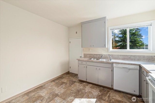 kitchen featuring stove, light countertops, dishwasher, a sink, and stone finish flooring