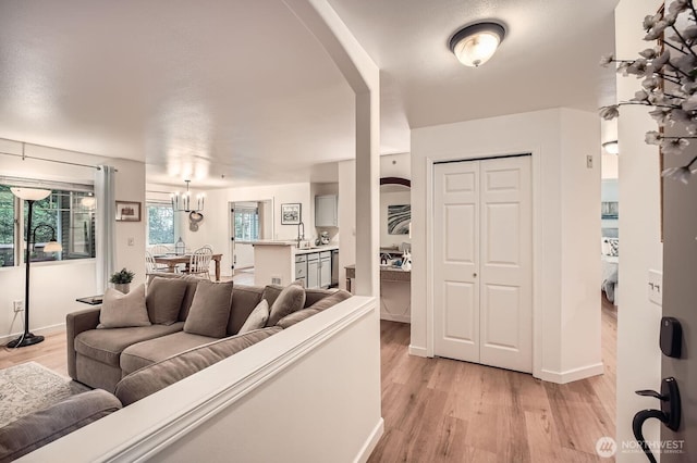 living area with baseboards, a chandelier, and light wood finished floors