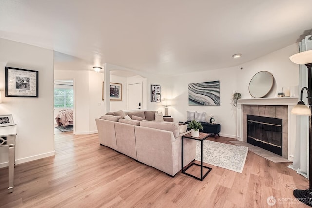 living area with a tiled fireplace, light wood-style floors, and baseboards