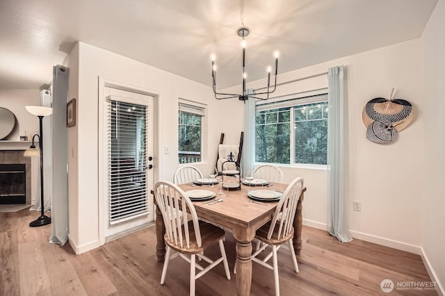 dining space featuring baseboards, a fireplace, light wood-type flooring, and a chandelier