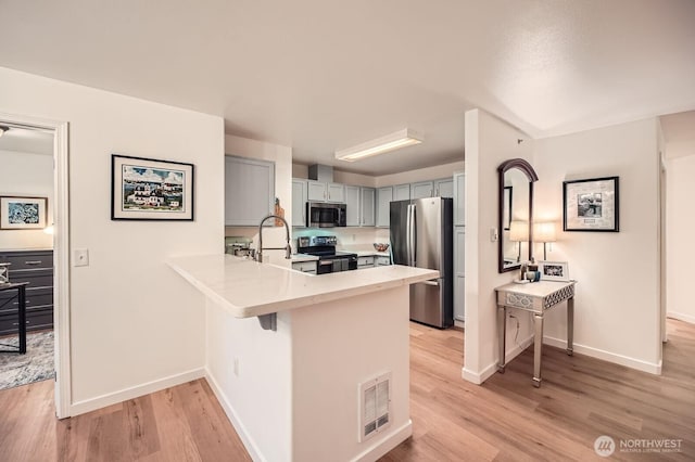 kitchen with visible vents, light countertops, light wood finished floors, a peninsula, and stainless steel appliances