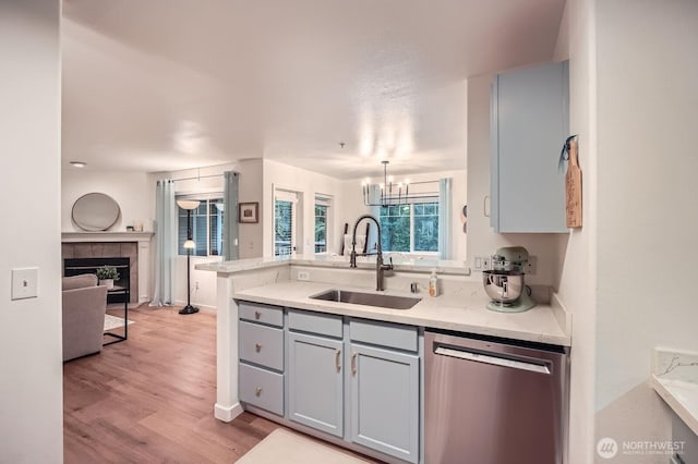 kitchen with gray cabinets, stainless steel dishwasher, a sink, a peninsula, and light wood-style flooring