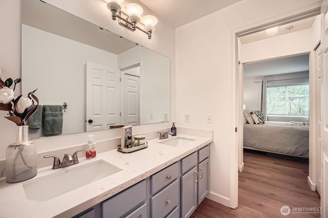 ensuite bathroom with double vanity, a sink, ensuite bath, and wood finished floors