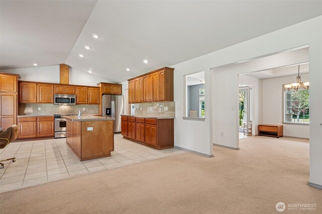 kitchen with brown cabinetry, an inviting chandelier, lofted ceiling, backsplash, and stainless steel appliances