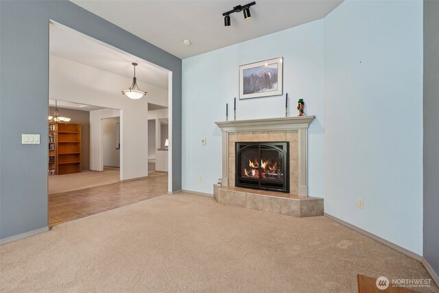 unfurnished living room featuring a tiled fireplace, tile patterned flooring, carpet floors, baseboards, and a notable chandelier