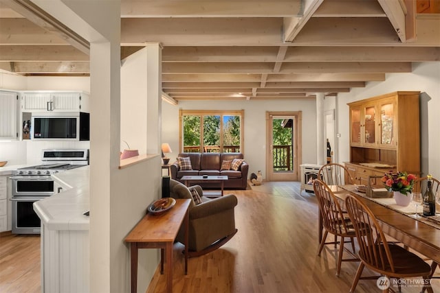 interior space with beamed ceiling, open floor plan, tile counters, light wood finished floors, and double oven range