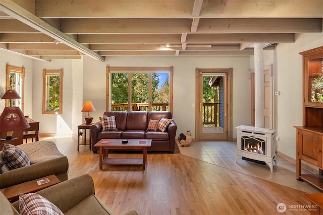 living room with a wood stove, light tile patterned flooring, a healthy amount of sunlight, and beamed ceiling
