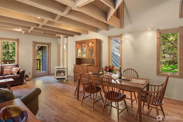 dining area featuring baseboards, beam ceiling, a wood stove, and light wood-type flooring
