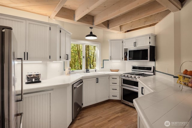 kitchen featuring a sink, tile counters, stainless steel appliances, backsplash, and beamed ceiling