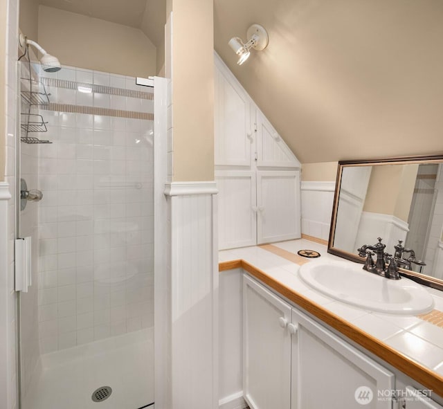bathroom with a shower stall, a wainscoted wall, lofted ceiling, and vanity