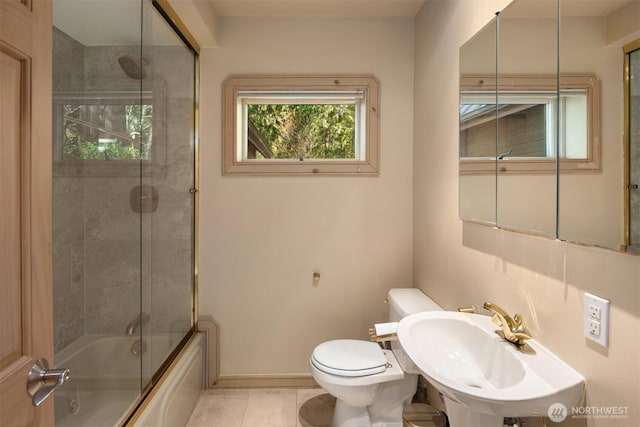 bathroom featuring tile patterned flooring, toilet, baseboards, a sink, and enclosed tub / shower combo