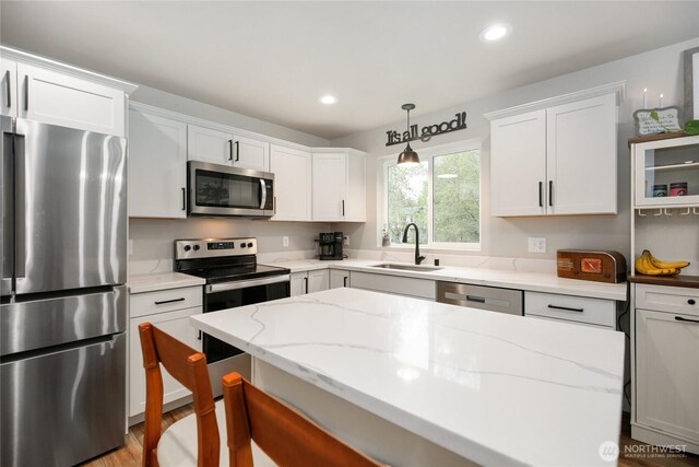 kitchen with a sink, pendant lighting, white cabinets, appliances with stainless steel finishes, and light stone countertops
