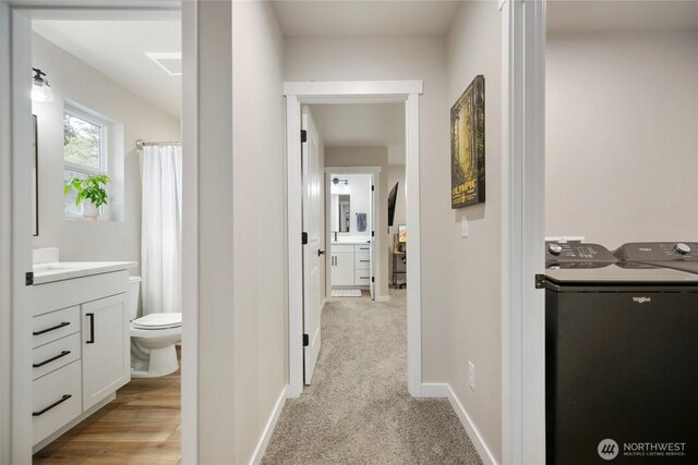 corridor featuring washing machine and dryer, baseboards, and light colored carpet