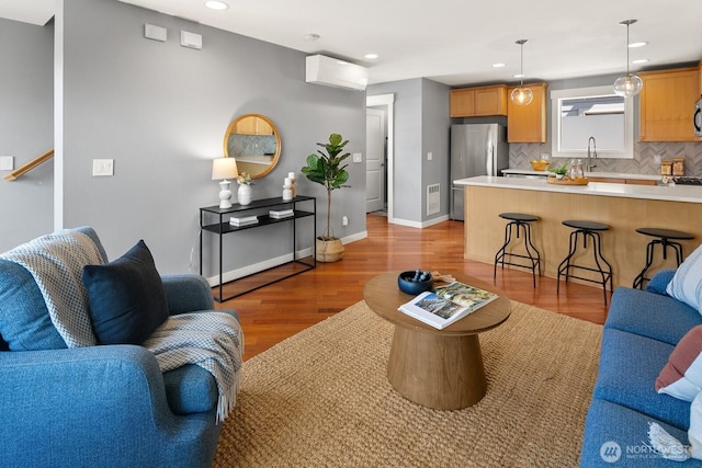 living room featuring an AC wall unit, light wood finished floors, baseboards, visible vents, and recessed lighting