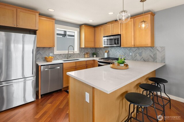 kitchen featuring a peninsula, a sink, appliances with stainless steel finishes, dark wood-type flooring, and a breakfast bar area