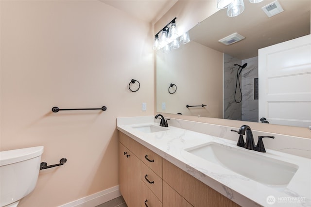bathroom featuring toilet, a shower, double vanity, and baseboards