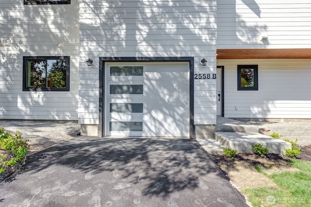 view of exterior entry featuring asphalt driveway and an attached garage