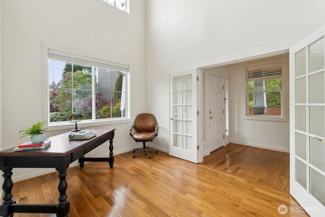 office area with baseboards, light wood-style flooring, and a towering ceiling