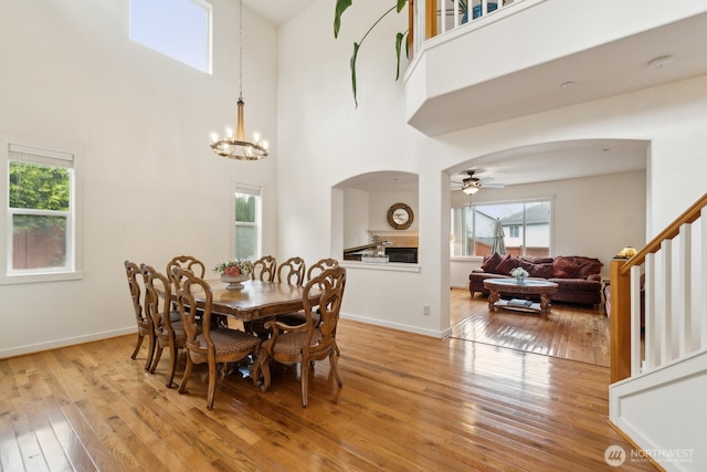dining room featuring arched walkways, light wood-style flooring, ceiling fan with notable chandelier, and a towering ceiling