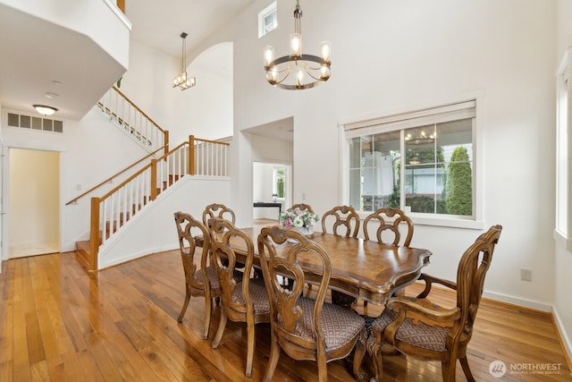 dining room featuring a high ceiling, an inviting chandelier, stairs, light wood-type flooring, and visible vents